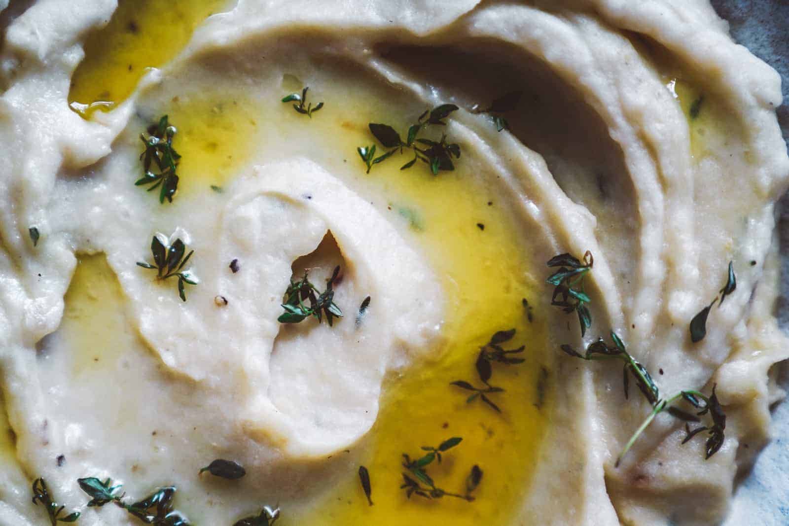 Close-up of creamy Onion Garlic Mashed Potatoes drizzled with olive oil, garnished with fresh thyme leaves.