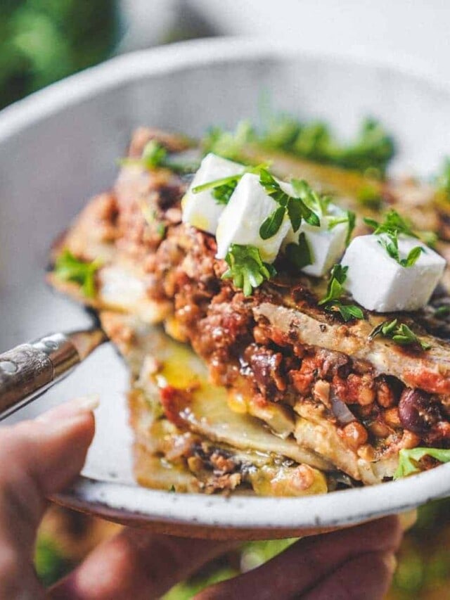 Big bowl of vegan moussaka ready to be eaten with fresh vegan feta and herbs.