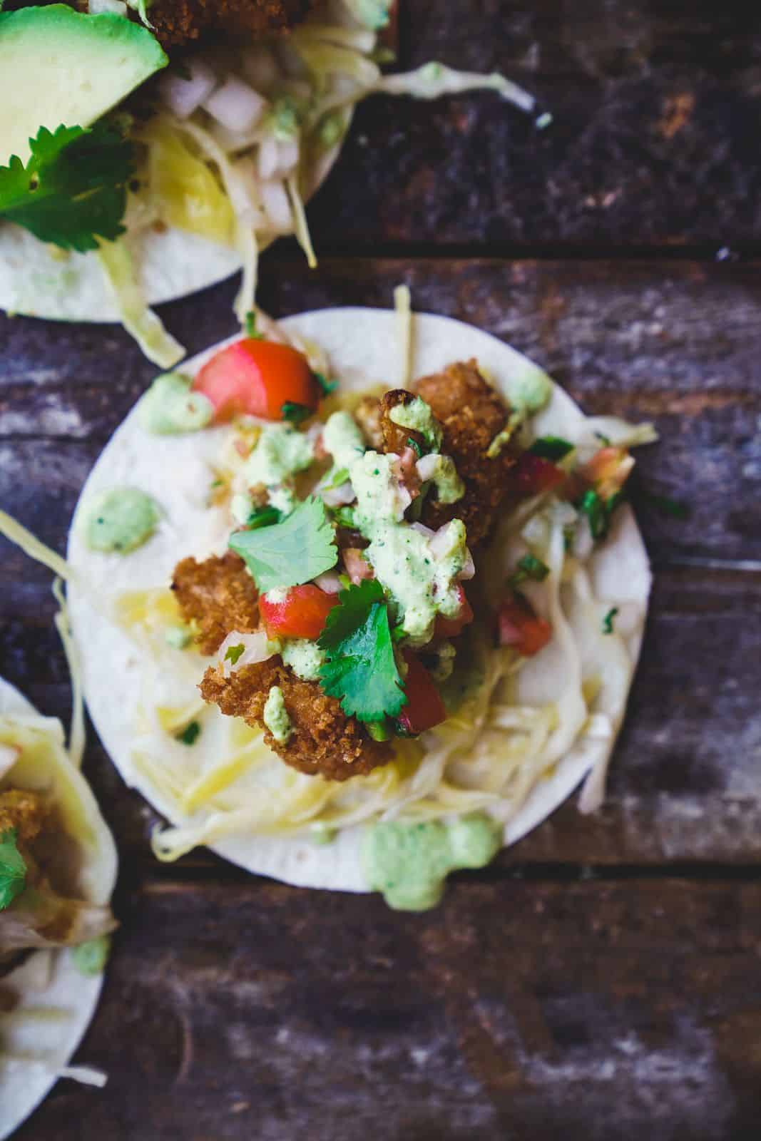 A taco filled with golden-brown crispy cauliflower pieces, topped with shredded cabbage, fresh pico de gallo, and a drizzle of creamy cilantro sauce