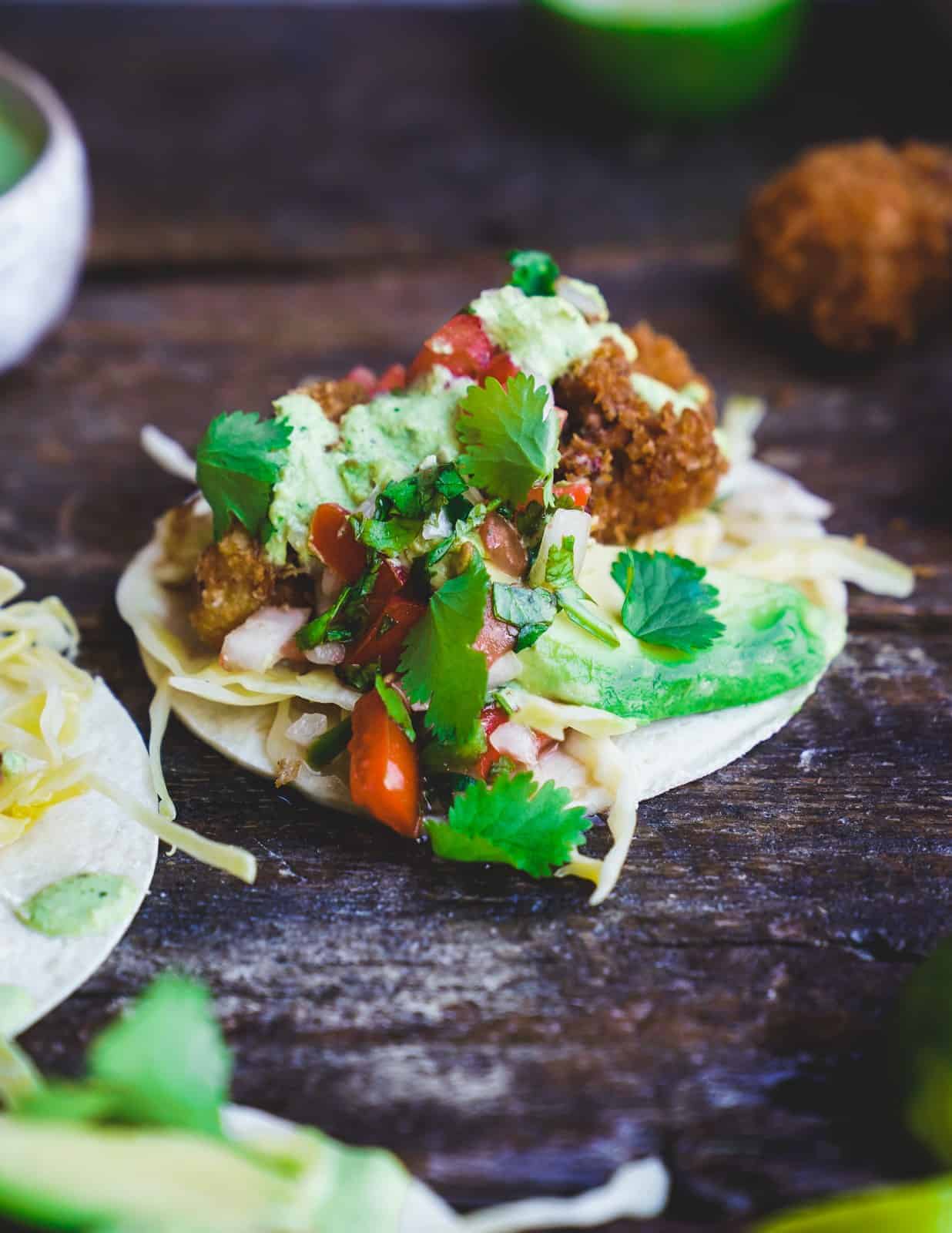 A taco filled with golden-brown crispy cauliflower pieces, topped with shredded cabbage, fresh pico de gallo, and a drizzle of creamy cilantro sauce