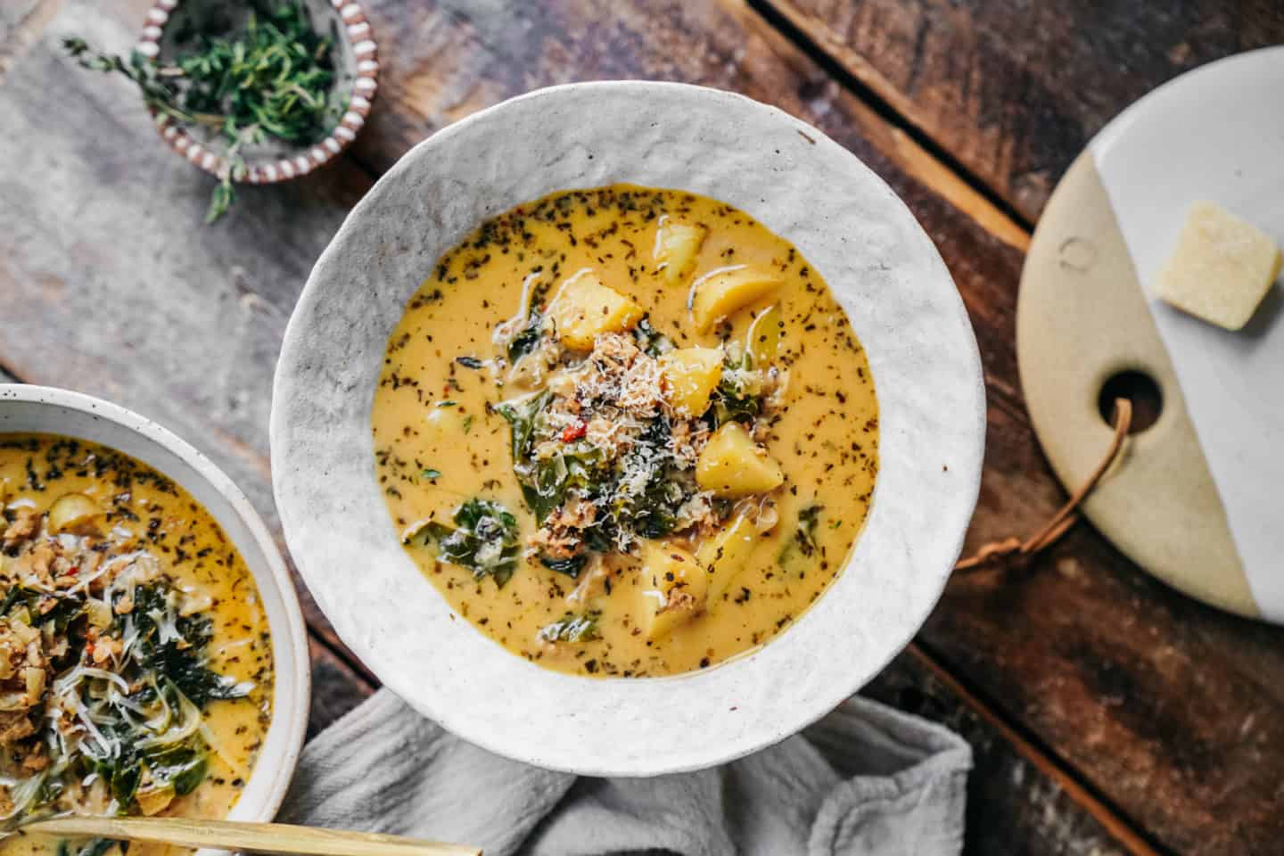 Creamy vegan zuppa toscana soup in a white bowl, showing chunks of golden potatoes, plant-based sausage crumbles, and bright green kale floating in a rich broth