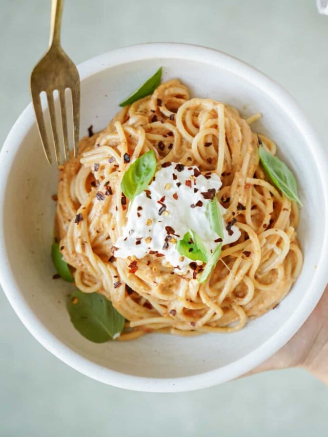 Hands holding a bowl of burrata pasta