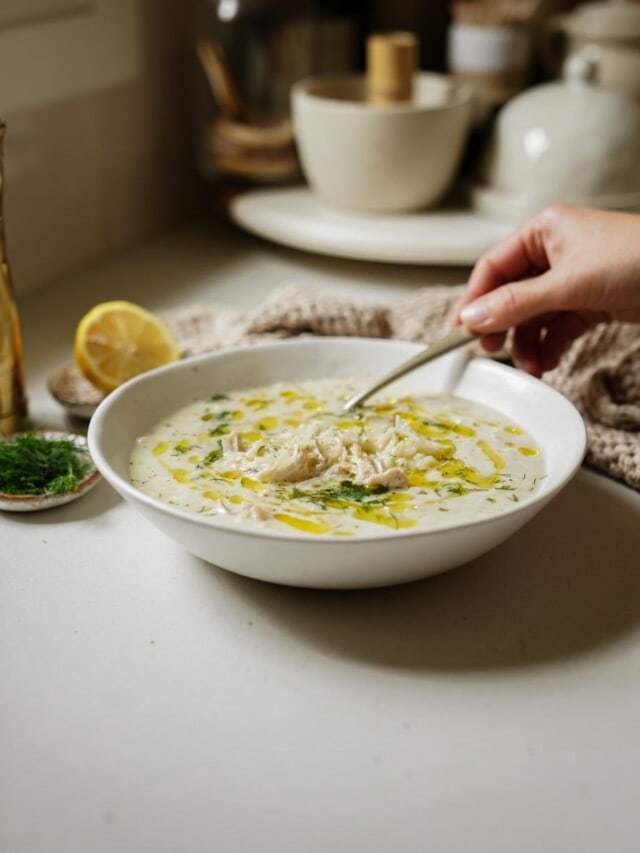 Avgolemono soup in a white bowl with a spoon in it