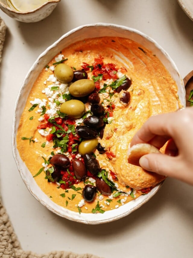 Close up of cracker being dipped in spicy feta dip