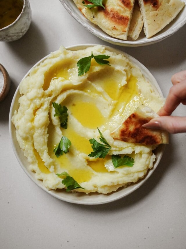 Skordalia in a bowl with bread dipping into it