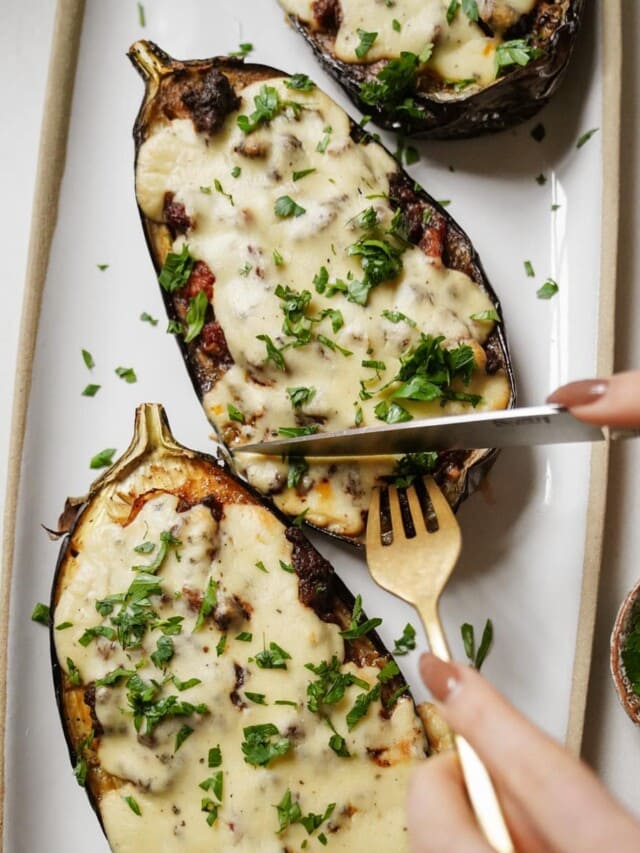 Knife and fork cutting into a stuffed eggplant