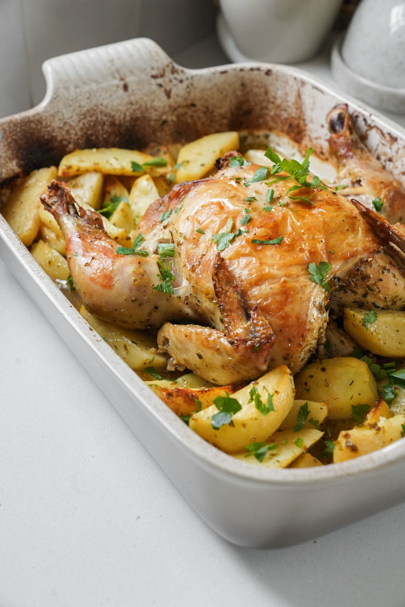 Whole roasted chicken in a casserole dish with potatoes