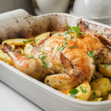 Whole roasted chicken in a casserole dish with potatoes