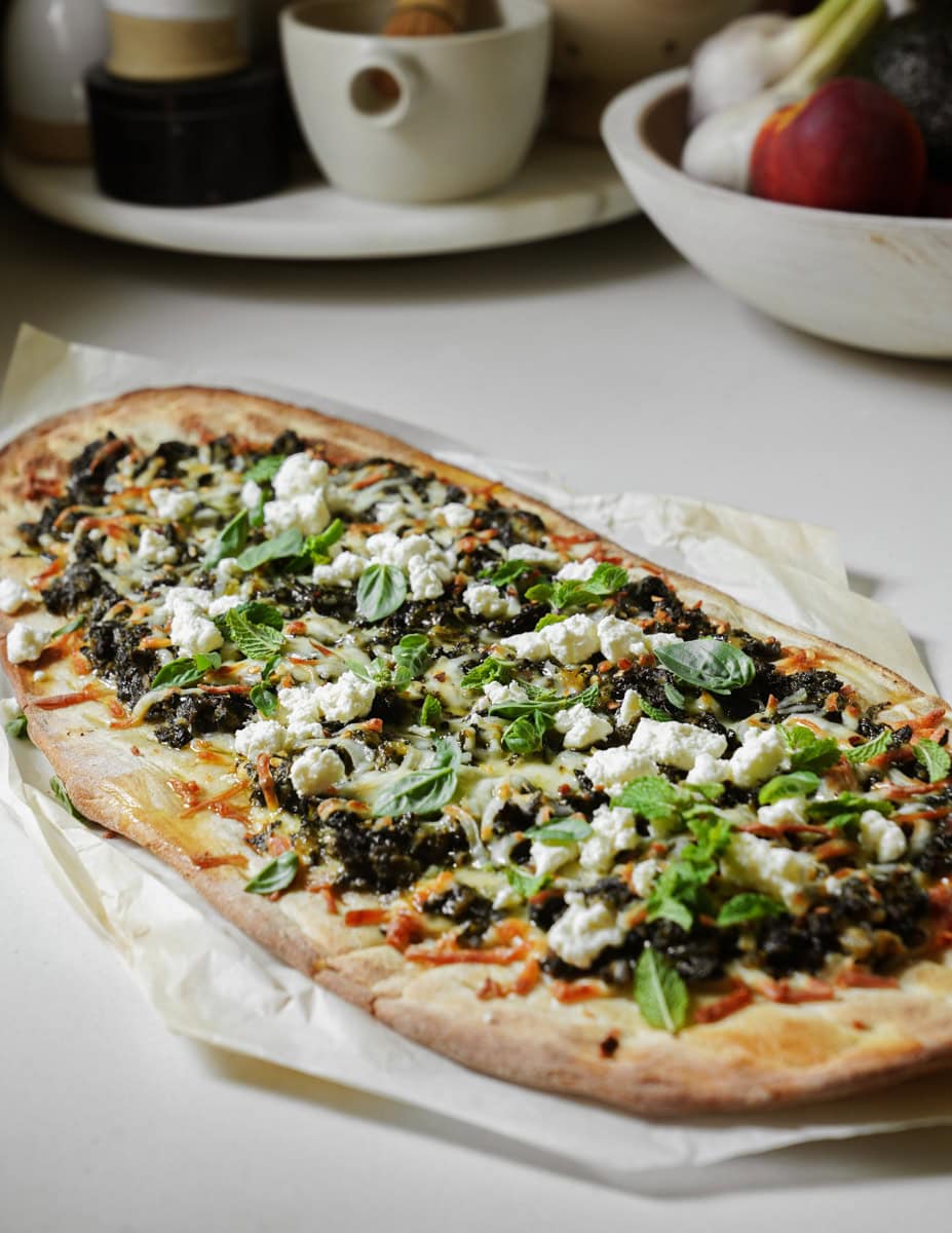 Greek flatbread on a counter topped with fresh herbs and feta