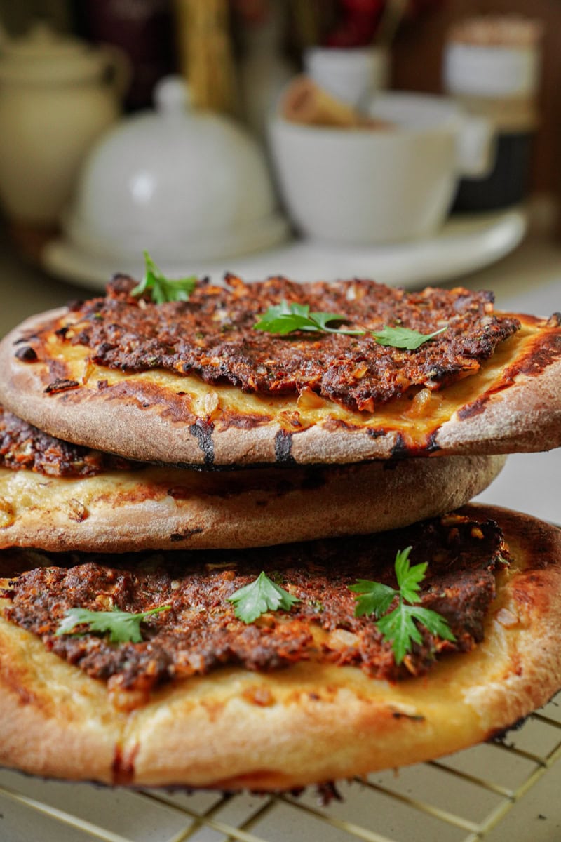 Three round, golden-brown Manakeesh flatbreads stacked on a cooling rack, topped with savory ground beef and a sprinkle of herbs.