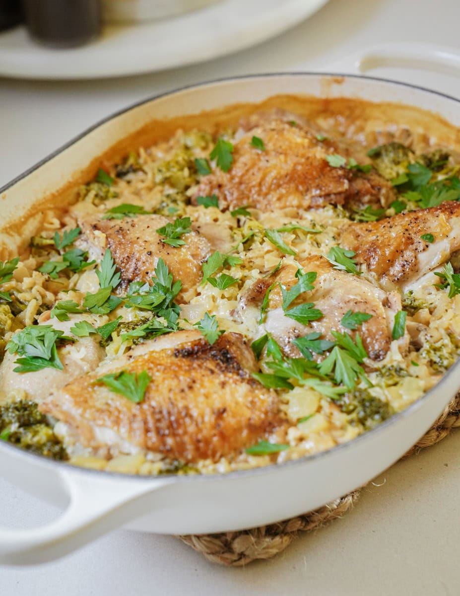 A white casserole dish showcasing tender pieces of chicken nestled among cheesy rice, with flecks of herbs visible throughout.