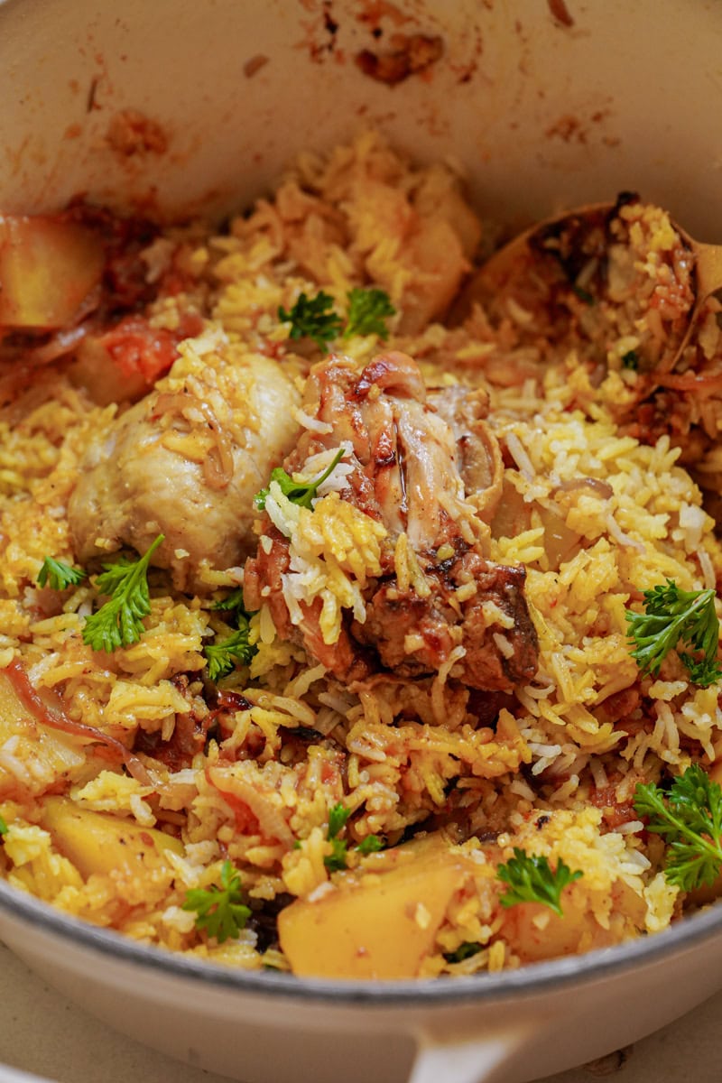 A close up of fragrant yellow rice, tender chicken pieces and flecks of herbs.