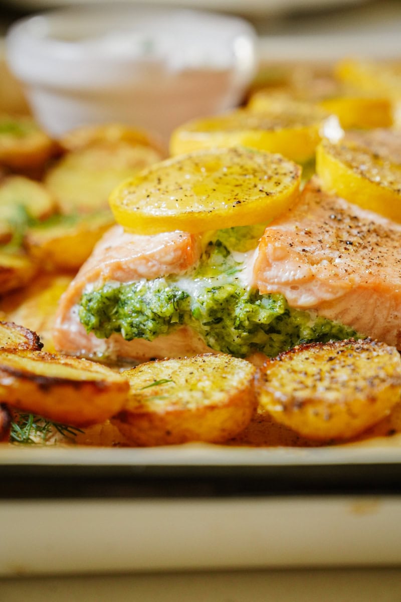 A salmon fillet rests on a bed of roasted potatoes. The salmon is partially opened, revealing a vibrant green stuffing of spinach, feta, and shrimp.