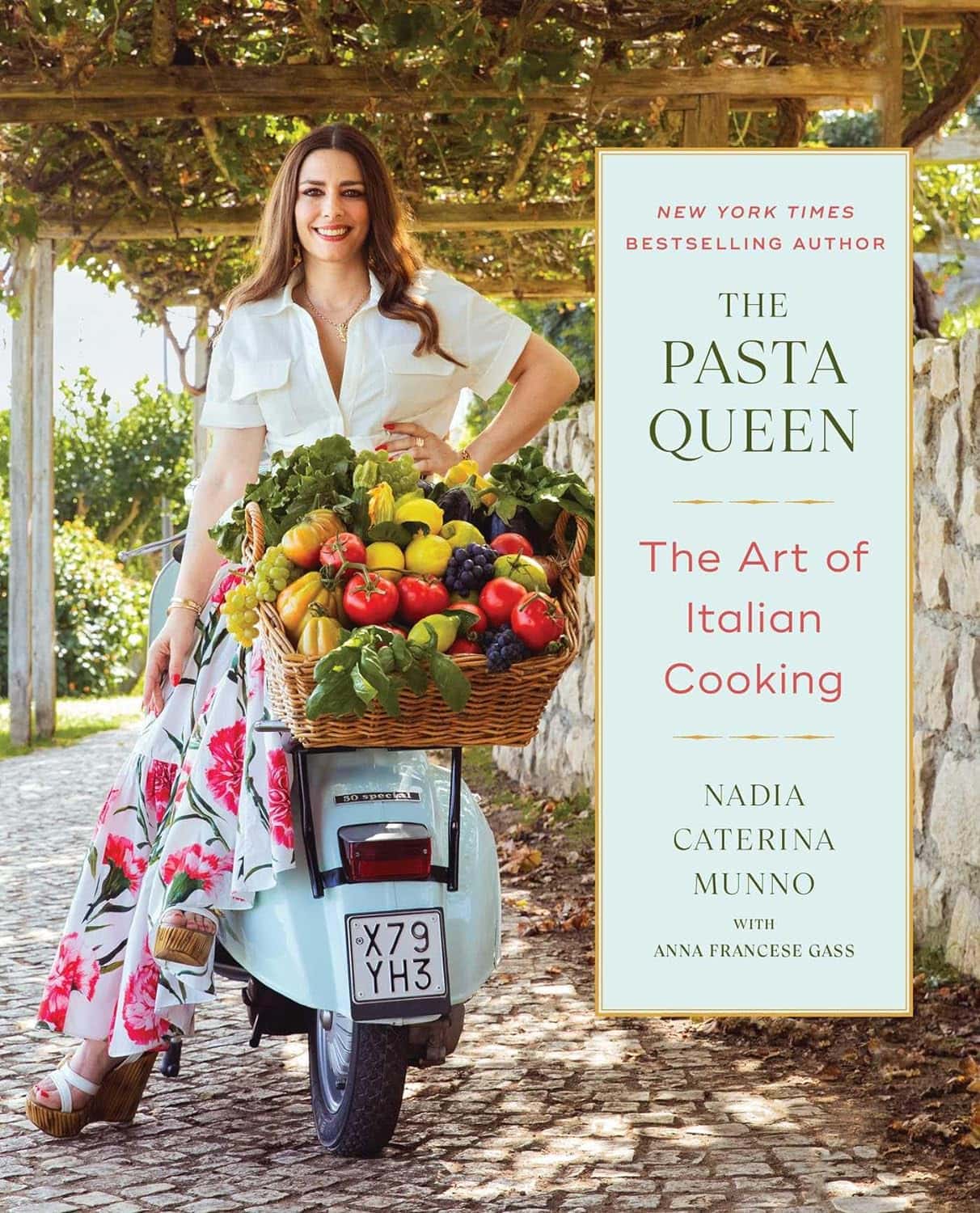 A smiling woman stands next to a vintage scooter, carrying a basket filled with fresh vegetables and herbs. Shes wearing a floral skirt and white blouse. A stone wall and lush greenery complete the scenic outdoor setting. Book title: The Pasta Queen.