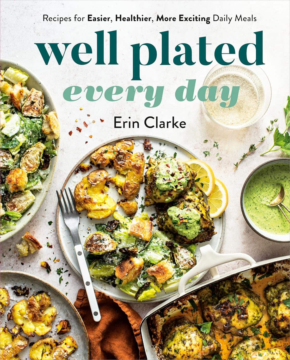 Cover of the cookbook Well Plated Every Day by Erin Clarke. The image displays various dishes, including roasted vegetables, chicken with green sauce, and a bread dish, all arranged appealingly in bowls and pans. A fork and lemon slices are visible.