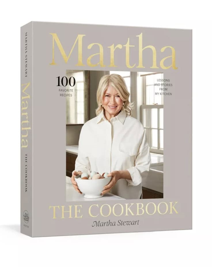 Cover of a cookbook titled Martha Stewart: The Cookbook. Features a woman holding a bowl of eggs in a kitchen setting. Text reads 100 Favorite Recipes and Lessons and Stories From My Kitchen.