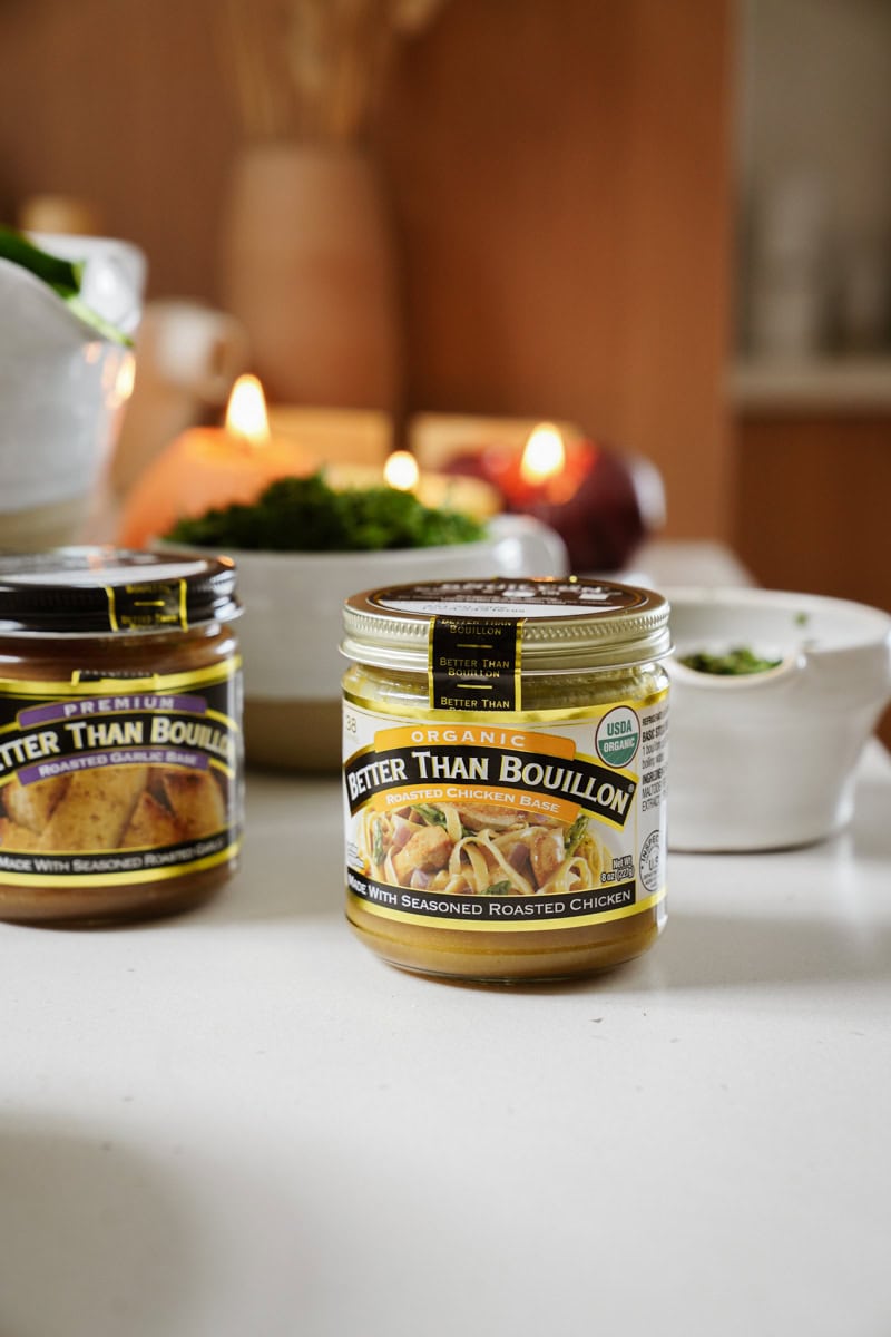 Two jars of Better Than Bouillon, one labeled Organic Roasted Chicken Base, are on a kitchen counter. A white bowl and other kitchen items are blurred in the background.