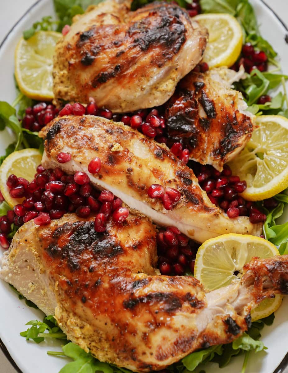 Grilled chicken pieces on a bed of arugula, garnished with lemon slices and pomegranate seeds.